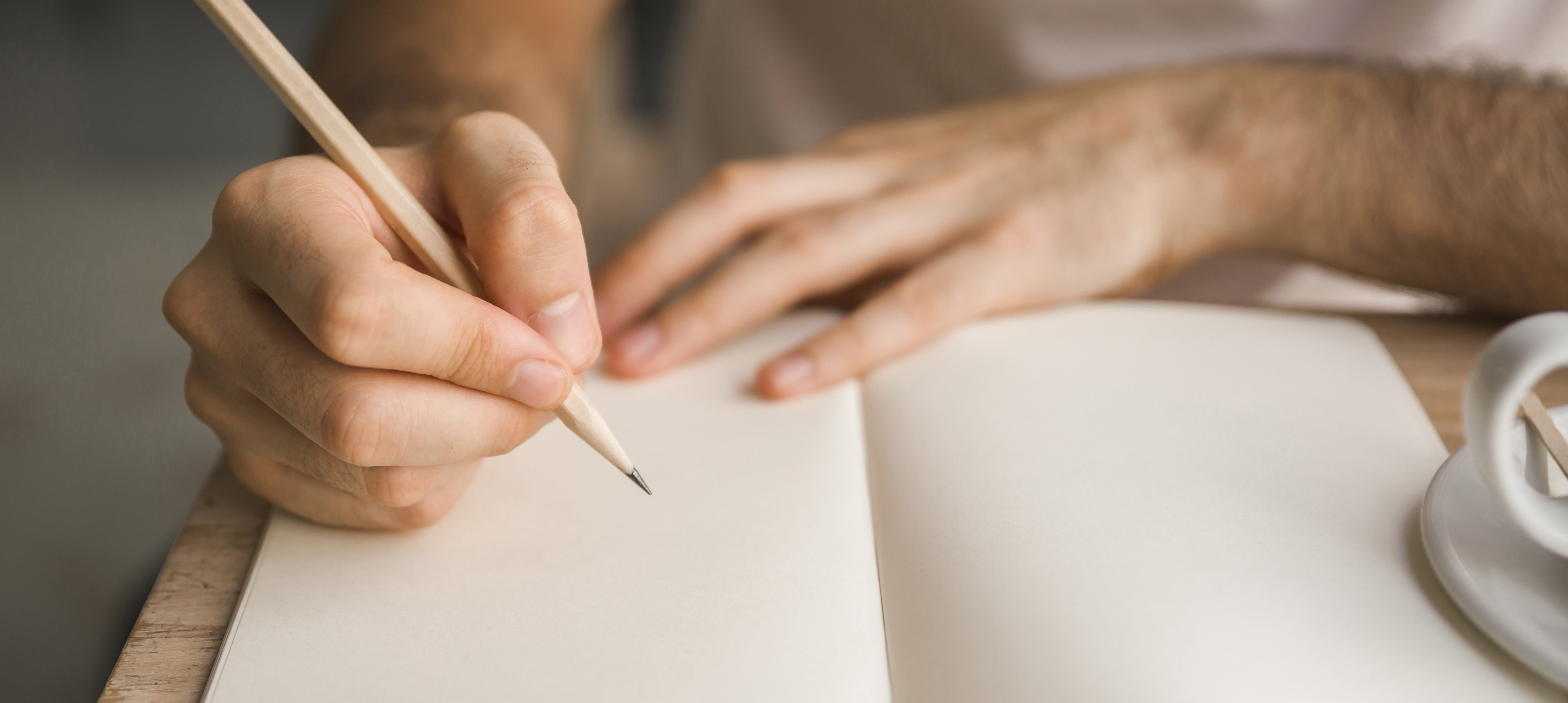 Hand beginnt mit Bleistift in ein weißes Buch zu schreiben