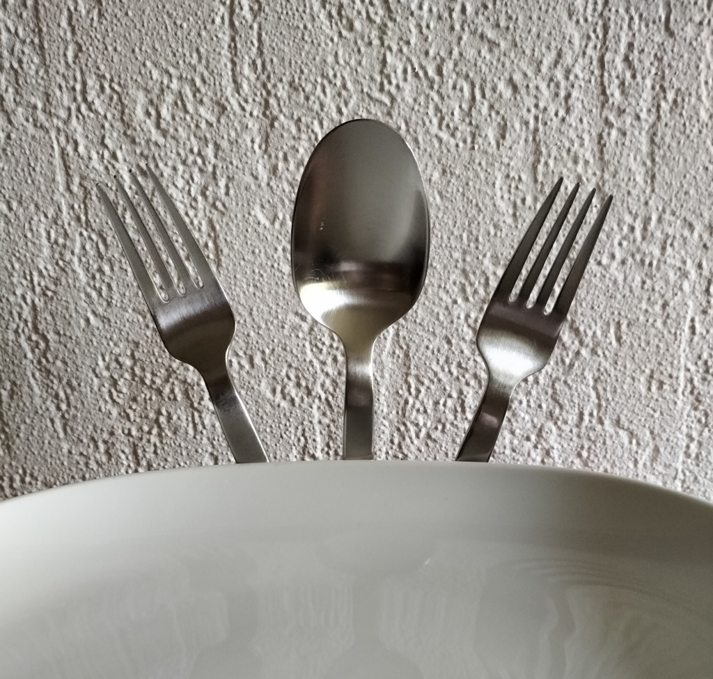 Zwei Gabel und ein Löffel ragen über einen Tellerrand hinaus