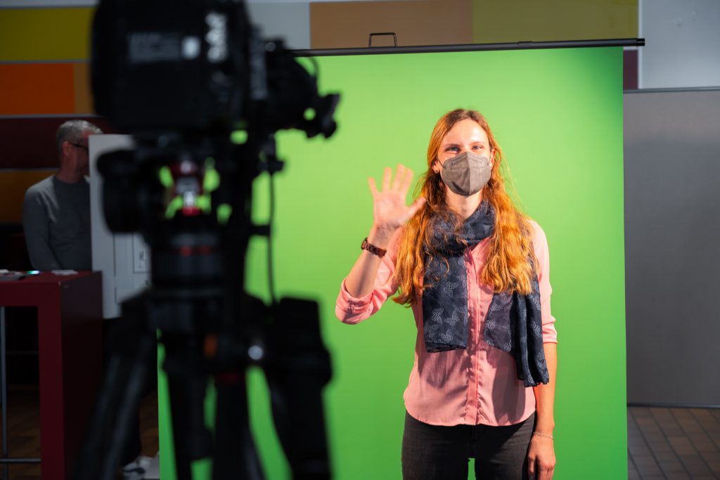 Person vor einem Green Screen winkt in die Kamera